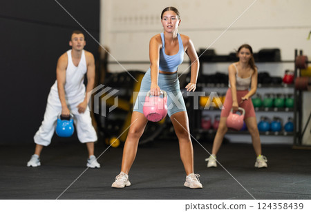 Sporty athletic woman in sportswear training with kettlebell in sport gym Sporty athletic woman in sportswear training with kettlebell in sport gym 124358439