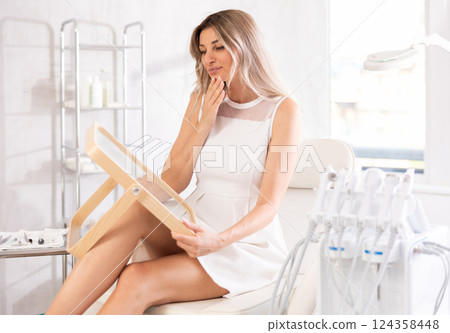 Young joyful woman examining her face after cosmetic procedure Young joyful woman examining her face after cosmetic procedure 124358448
