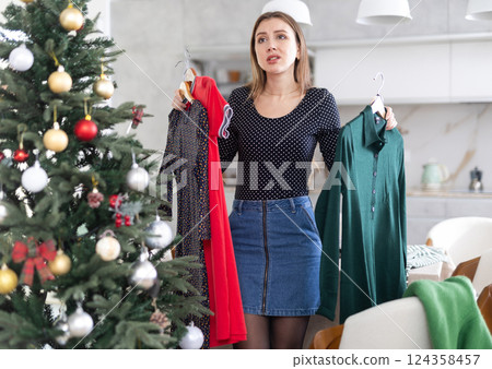 Young upset woman choosing which dress to wear Young upset woman choosing which dress to wear 124358457
