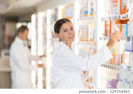 Young female pharmacist putting medical product on shelf in drugstore Young female pharmacist putting medical product on shelf in drugstore 124358465