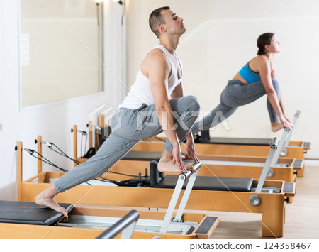 Sporty man in sports wear engages in Pilates on reformer machine 124358467