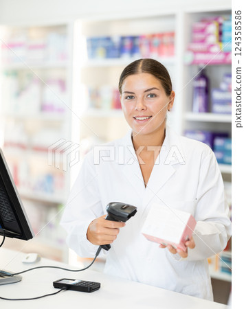Young female pharmacist scanning barcode on sold medicine box Young female pharmacist scanning barcode on sold medicine box 124358586