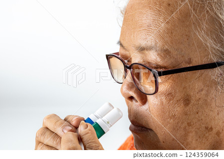 haler therapy: An anxious elderly asian woman with glasses holds two inhalers carefully near her nostrils. 124359064