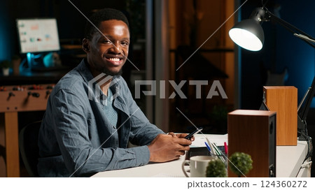 Portrait of african american guy scrolling on his mobile phone at home, takes break from his freelance tasks and online work. Young adult texting messages on social media app, relaxation. Camera B. Portrait of african american guy scrolling on his mobile phone at home, takes break from his freelance tasks and online work. Young adult texting messages on social media app, relaxation. Camera B. 124360272