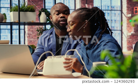 African American angry woman pulling out the LAN cable from the router while her partner reads a technical manual for troubleshooting. Couple getting mad and arguing over signal loss. Camera B. African American angry woman pulling out the LAN cable from the router while her partner reads a technical manual for troubleshooting. Couple getting mad and arguing over signal loss. Camera B. 124360293