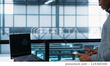 Technician in data center with laptop and tablet integrating AI driven automation tools. Server room worker using artificial intelligence on devices, ensuring continuous uptime, camera A 124360300