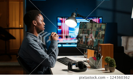 Black guy meeting with group of individuals on web video conference, uses technology for virtual communication. Freelancer working remotely, online meetings or classes in a cozy home. Camera B. 124360362