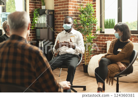 Young black man seated in brick wall office, sharing his depression recovery process at group therapy session. African american guy siting in circle and talking about mental health with aa community. 124360381