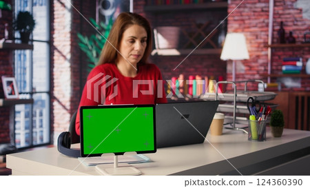 Mature woman reading forms and papers next to isolated screen and studying handwritten notes, surfing the web and staying connected for her freelance work tasks. Multitasking online. Camera B. Mature woman reading forms and papers next to isolated screen and studying handwritten notes, surfing the web and staying connected for her freelance work tasks. Multitasking online. Camera B. 124360390