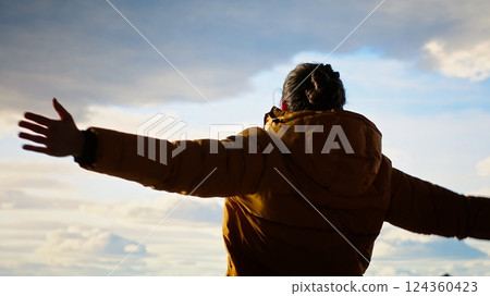 Cheerful hiker celebrates climbing the rugged wilderness with a victory dance, feeling proud of his personal achievement. Nature lover enjoying the lovely mountain landscape. Camera B. 124360423