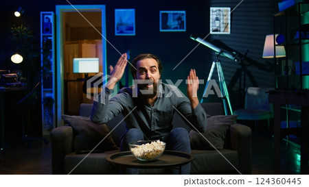 Supporter watching sports match on live broadcast, raging on couch in anger seeing team mistake. Angry man looking at football competition fuming, releasing pent up emotions, camera B Supporter watching sports match on live broadcast, raging on couch in anger seeing team mistake. Angry man looking at football competition fuming, releasing pent up emotions, camera B 124360445