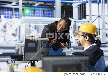 Man and woman working in photovoltaics factory optimizing production flow. African american manager in sustainable energy solar panels plant monitoring manufacturing process on computer 124360497