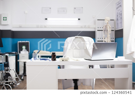 Organized, empty hospital room with desk, chair, and healthcare technology for efficient patient care. Modern, clean doctors office having a laptop and medical equipment on white table. 124360541