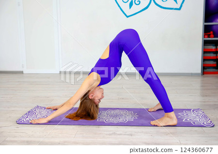 Woman practicing downward-facing dog yoga pose in a studio 124360677