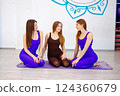 Three women sitting on a yoga mat in a studio 124360679