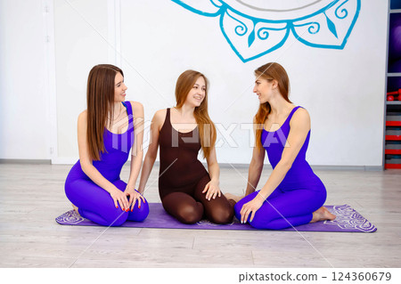 Three women sitting on a yoga mat in a studio Three women sitting on a yoga mat in a studio 124360679