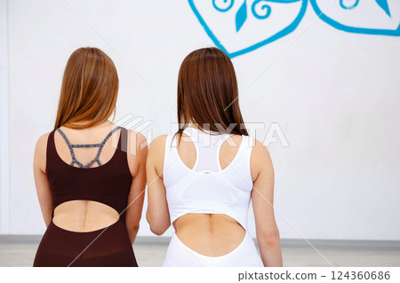 Back view of two women in stylish open-back bodysuits 124360686