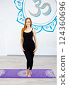 Smiling woman in black sportswear standing on a yoga mat  124360696