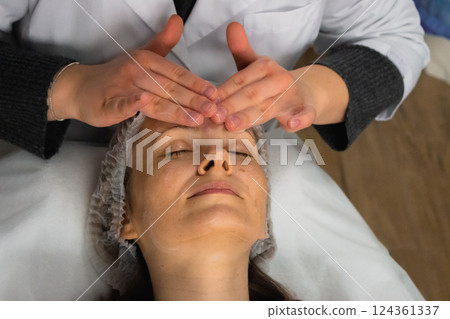 Foam cleaning and face massage in beauty salon. Smiling woman relaxing with anti-aging massage. Wellness procedure. Skincare treatment. Cosmetologist hands over client face. Healthcare pleasure. Foam cleaning and face massage in beauty salon. Smiling woman relaxing with anti-aging massage. Wellness procedure. Skincare treatment. Cosmetologist hands over client face. Healthcare pleasure. 124361337
