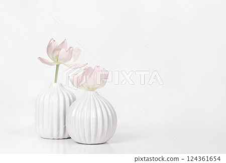 Two white textured vases with pink fading tulip flowers on white table Two white textured vases with pink fading tulip flowers on white table 124361654