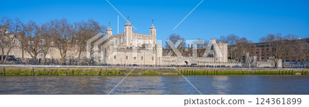 Tower Wharf showcases the historic Tower of London along the River Thames. Visitors admire the architecture and serene riverside view, enjoying a sunny, clear day in London. 124361899