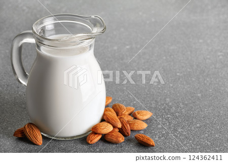 Fresh almond milk in glass pitcher stand on gray background with nuts scattered around it, creating visually appealing scene that promotes healthy eating and vegan alternatives Fresh almond milk in glass pitcher stand on gray background with nuts scattered around it, creating visually appealing scene that promotes healthy eating and vegan alternatives 124362411