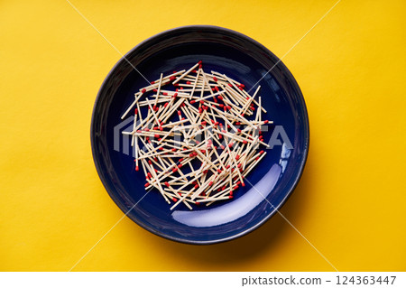 Matches in dark blue bowl over yellow background 124363447