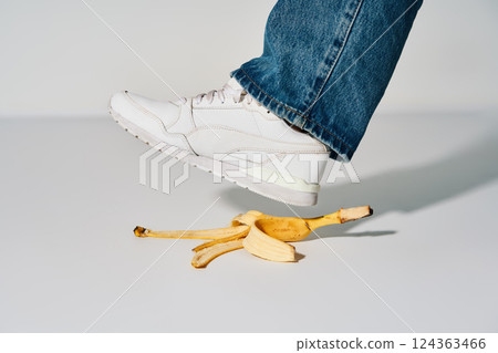 Foot stepping on banana peel over white background, 124363466