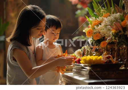 Mother and child participate in Vesak ritual, offering vibrant flowers to Buddha Mother and child participate in Vesak ritual, offering vibrant flowers to Buddha 124363923