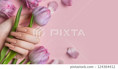 Woman hand with perfect nude manicure holding tulip flowers on pink background Woman hand with perfect nude manicure holding tulip flowers on pink background 124364412