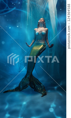 Mysterious elegant young woman, mermaid with golden tail, covered in flying fabric, floating against dreamlike ocean background 124364588