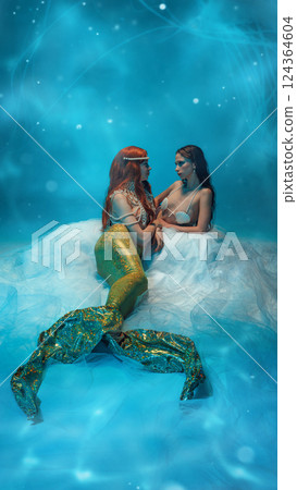 Intense gaze and deep conversation. Two young women, mermaids resting on transparent veil and gazing at each other 124364604