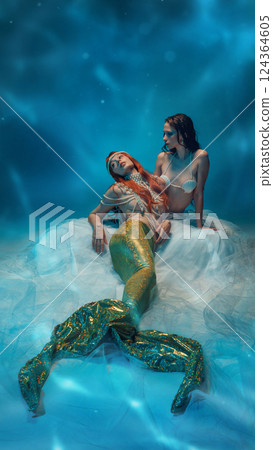 Serene mermaids resting on soft waves, surrounded by glowing blue reflections. Two young women expressing calmness and coziness. 124364605