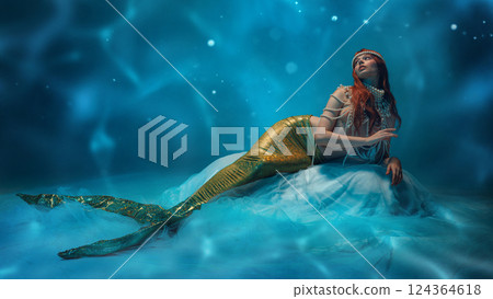 Beautiful redhaired woman, mermaid resting on soft waves, gazing into the distance with mystery and elegance. Beautiful redhaired woman, mermaid resting on soft waves, gazing into the distance with mystery and elegance. 124364618