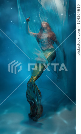 Flying towards dreams. Graceful young woman, redhaired mermaid elegantly covered in transparent veil, dancing against blue ocean-like background. 124364619