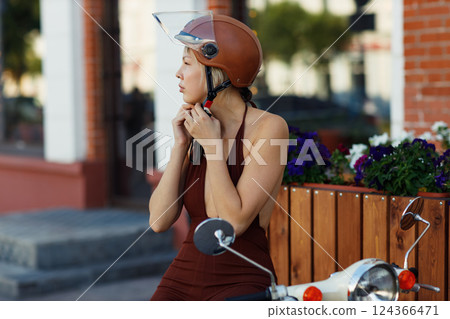Young woman put on helmet and riding on motorbike moped scooter in city street Young woman put on helmet and riding on motorbike moped scooter in city street 124366471