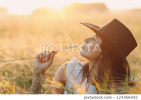 Woman farmer in cowboy hat profile portrait with spikelet at agricultural field on sunset. Woman farmer in cowboy hat profile portrait with spikelet at agricultural field on sunset. 124366492