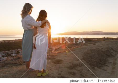 Mother and daughter embracing while watching golden sunset over coastal landscape Mother and daughter embracing while watching golden sunset over coastal landscape 124367108