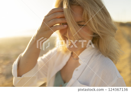 Blonde woman touching hair in golden sunlight at sunset Blonde woman touching hair in golden sunlight at sunset 124367136