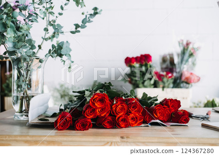 Red rose bouquet ready for packing in florist studio with eucalyptus in vase. Reflects monthly floral subscriptions and romantic gifting rituals 124367280