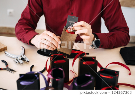 Male artisan packaging handmade jewelry in elegant ribbon gift bags, emphasizing branding through unboxing experience. Packaging as brand experience, unboxing trend, customer engagement. Male artisan packaging handmade jewelry in elegant ribbon gift bags, emphasizing branding through unboxing experience. Packaging as brand experience, unboxing trend, customer engagement. 124367363