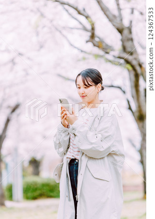 一名年輕女子用智慧型手機拍攝一排櫻花樹 124367533