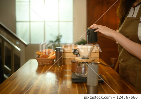 Close up of woman pouring hot water into a coffee dripper on a wooden kitchen counter Close up of woman pouring hot water into a coffee dripper on a wooden kitchen counter 124367666