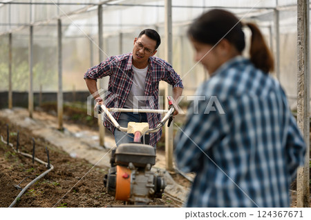 Male farmer works with a cultivator machine to prepare the soil in a greenhouse Male farmer works with a cultivator machine to prepare the soil in a greenhouse 124367671