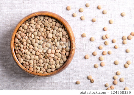 Large green lentils in a wooden bowl on linen fabric. Unshelled, dried plate lentils, a typically larger, flat variety of lentils, that hold their shape when cooked, used in soups, stews, or salads. Large green lentils in a wooden bowl on linen fabric. Unshelled, dried plate lentils, a typically larger, flat variety of lentils, that hold their shape when cooked, used in soups, stews, or salads. 124368329