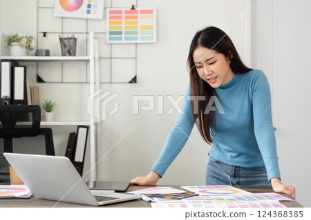 Creative Work and Design Process. A woman engaged in the creative design process, exploring color palettes and ideas in a modern workspace. 124368385