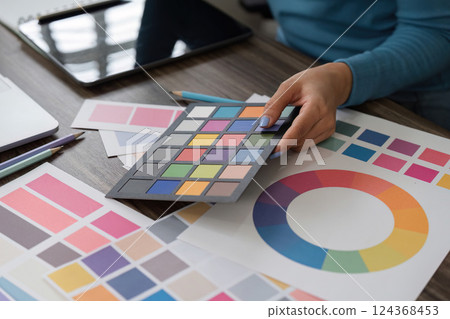 Color Selection and Artistic Design. A hand selecting color swatches for a creative project on a wooden workspace. 124368453