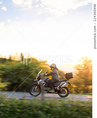 Motorcyclist rides through beautiful sunset landscape. Motorcyclist rides through beautiful sunset landscape. 124368996