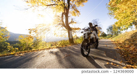Motorcyclist rides through scenic autumn forest trail. 124369000