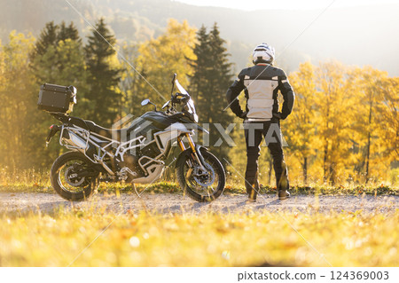 Motorcyclist stays in scenic autumn forest trail. 124369003